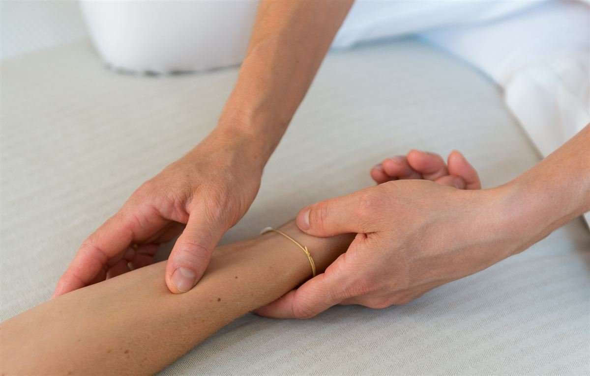 Zwei Hände bei einer achtsamen Berührung am Handgelenk mit einem Armband mit der Aufschrift Glück
