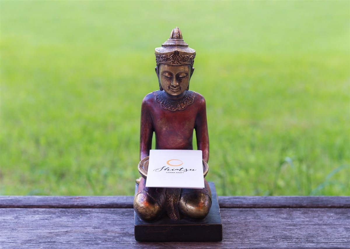 Kleine Buddha-Figur im Garten mit einer Visitenkarte von Shiatsu Carina Kraft